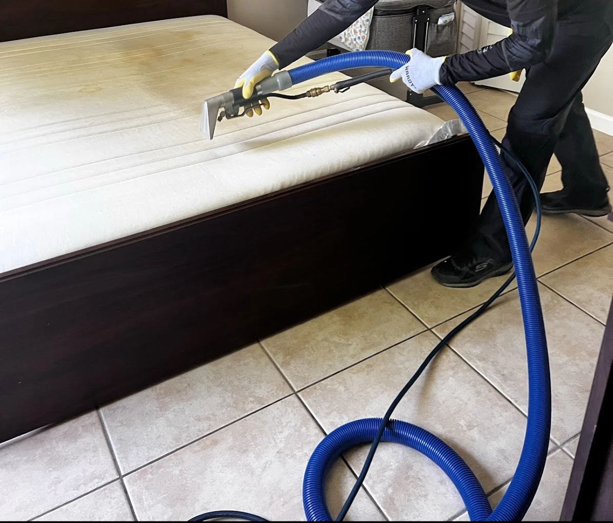 Technician steam cleaning a mattress in a bedroom